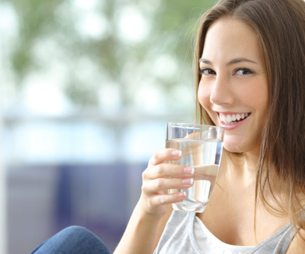Girl drinking water sitting on a couch at home and looking at camera